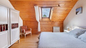 Una camera da letto con soffitto spiovente, una finestra, un letto, una sedia e un armadio.