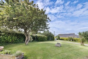 A garden with a large tree, a wooden planter, and a building in the background. - Ty kreiz – 500 m from the beach (Plomodiern)