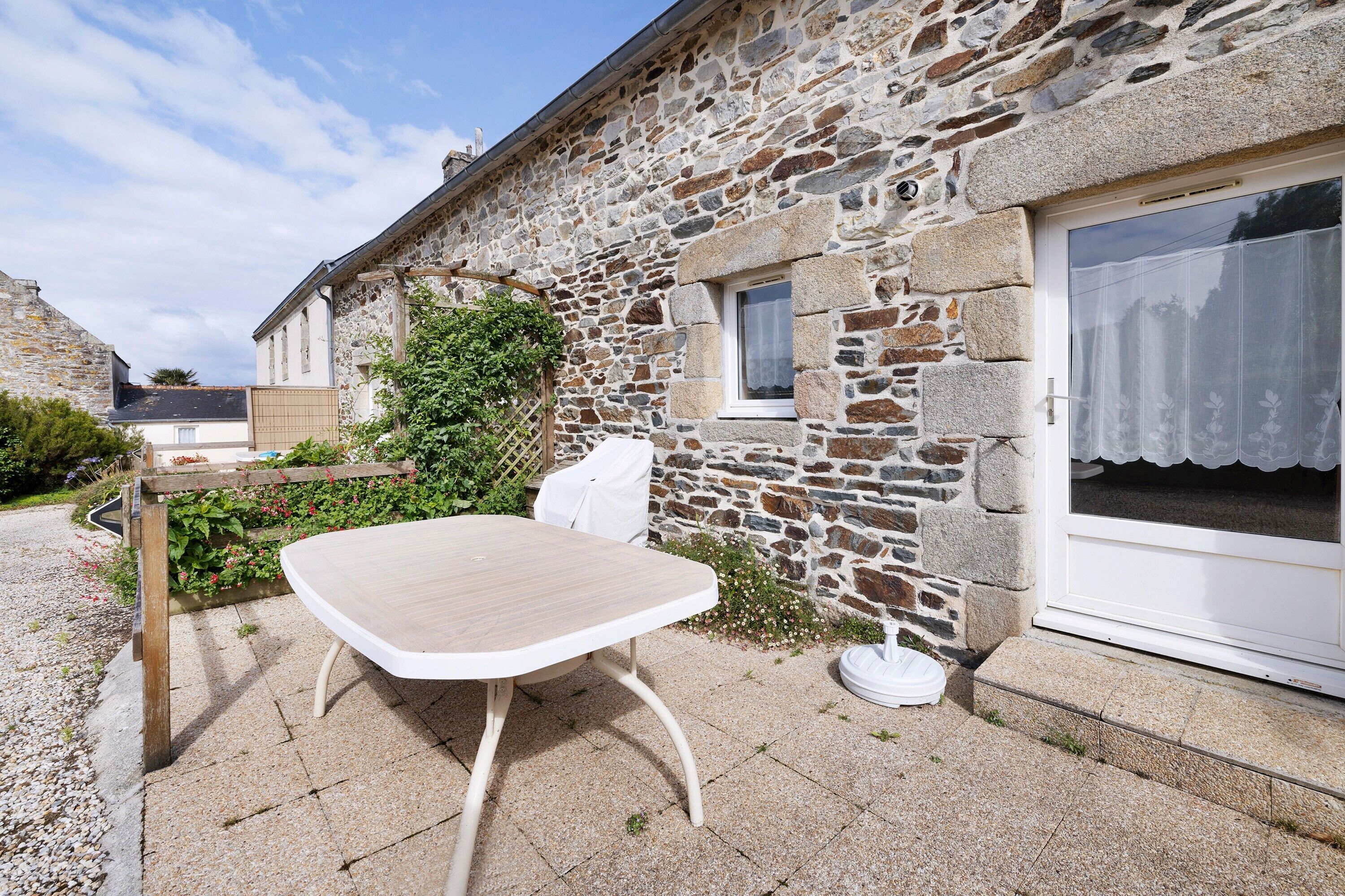 Un bâtiment en pierre avec une table en bois et une chaise blanche à l’extérieur.