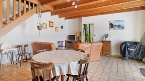 Zona pranzo con tavolo rotondo, sedie di legno, una scala e un televisore.