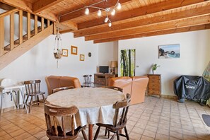 A dining area with a round table, wooden chairs, a staircase, and a TV. - Ty kreiz – 500 m from the beach (Plomodiern)