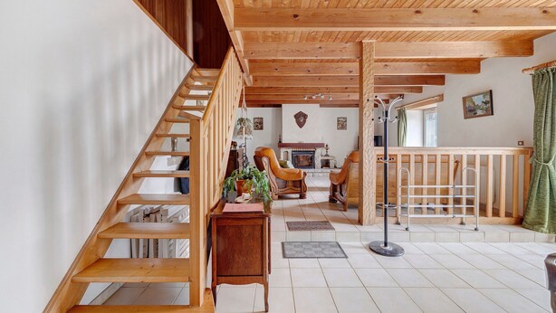 Eine Holztreppe führt zu einem Wohnbereich mit Kamin, Sitzgelegenheiten und Blick ins Freie.