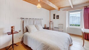 Ein Schlafzimmer mit Holzbalkendecke, einem Bett mit gemustertem Überwurf, einem Nachttisch mit Lampe und einem Fenster mit Vorhängen.