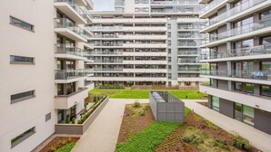 Un immeuble résidentiel moderne à plusieurs étages, doté de balcons, d’une cour intérieure et d’un jardin sur le toit.