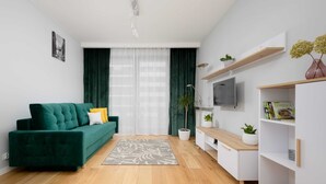 Un salon moderne avec un canapé vert, un téléviseur à écran plat, une table basse en bois et une étagère blanche.