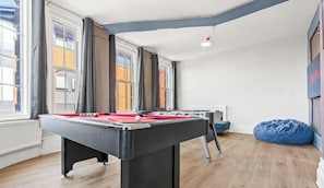 A room with a foosball table, a blue bean bag, and a window with curtains. - Melissa`s Central Stay (Nottingham)