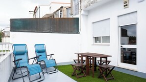 En terrasse med blå stole og et træbord, omgivet af kunstgræs.