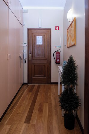 Un couloir avec une porte en bois, un extincteur, un petit sapin de Noël et un luminaire fixé au mur.