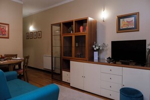 A living room with a sofa, a dining table, a cabinet with glass doors, and a television. - RH Charming Apartment São Victor (Braga)