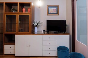 Ein Wohnzimmer mit Fernseher auf einem Schrank, einer Vitrine und einem blauen Hocker.