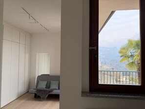 Ein Zimmer mit Bett, Schrank, Fenster mit Bergblick und Balkon mit Geländer.