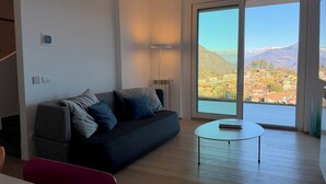 Ett modernt vardagsrum med en soffa, ett litet bord och utsikt över ett bergigt landskap genom stora fönster.