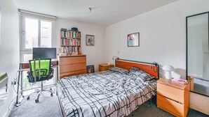 A bedroom with a bed, a desk with a chair, a bookshelf, a nightstand, and a window. - Comfortable 1 bed Near Deptford Station (London)