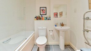 A small bathroom with a glass shower enclosure, a white toilet, a pedestal sink, and a mirror above the sink. - Comfortable 1 bed Near Deptford Station (London)
