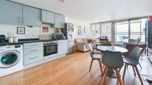 A modern kitchen with a washing machine, dining area with chairs, and a large window. - Comfortable 1 bed Near Deptford Station (London)