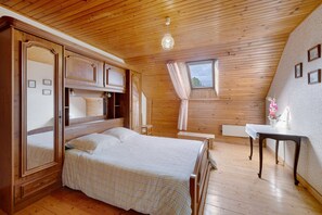 Une chambre avec un plafond en bois, un lit, une table de chevet, une fenêtre avec des rideaux et une étagère fixée au mur.