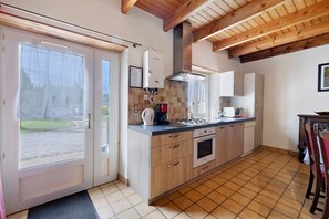 Une cuisine avec des meubles en bois, un four encastré, une machine à café et une fenêtre donnant sur un jardin.