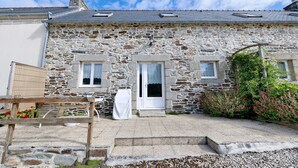 A stone building with a white door, two windows, and a small garden with flowers. - Ty izella – 500m from the sea (Plomodiern)