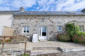 Un bâtiment en pierre avec une porte blanche, deux fenêtres et un petit jardin fleuri.