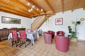 Un coin repas avec un escalier en bois, une table entourée de chaises et des plantes en pot.