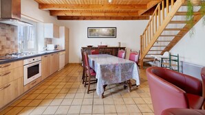 A kitchen with wooden beams, a dining table with chairs, a red sofa, and a staircase. - Ty izella – 500m from the sea (Plomodiern)