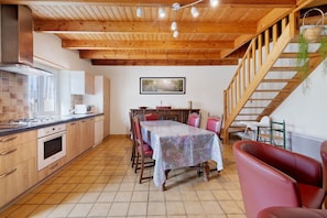 Une cuisine avec des poutres en bois, une table à manger avec des chaises, un canapé rouge et un escalier.