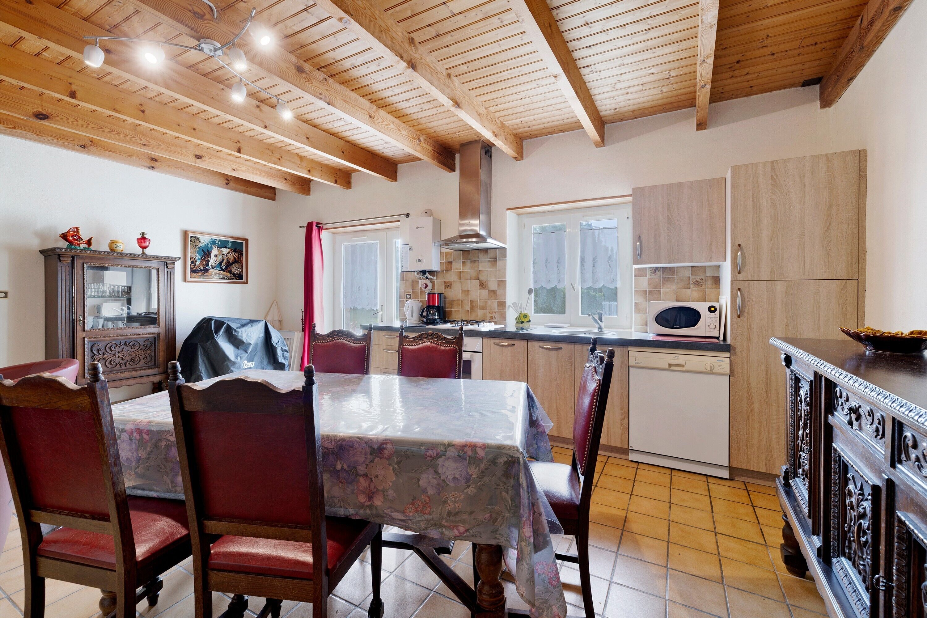 Una cocina con vigas de madera, una mesa de comedor con sillas, lavavajillas y microondas.
