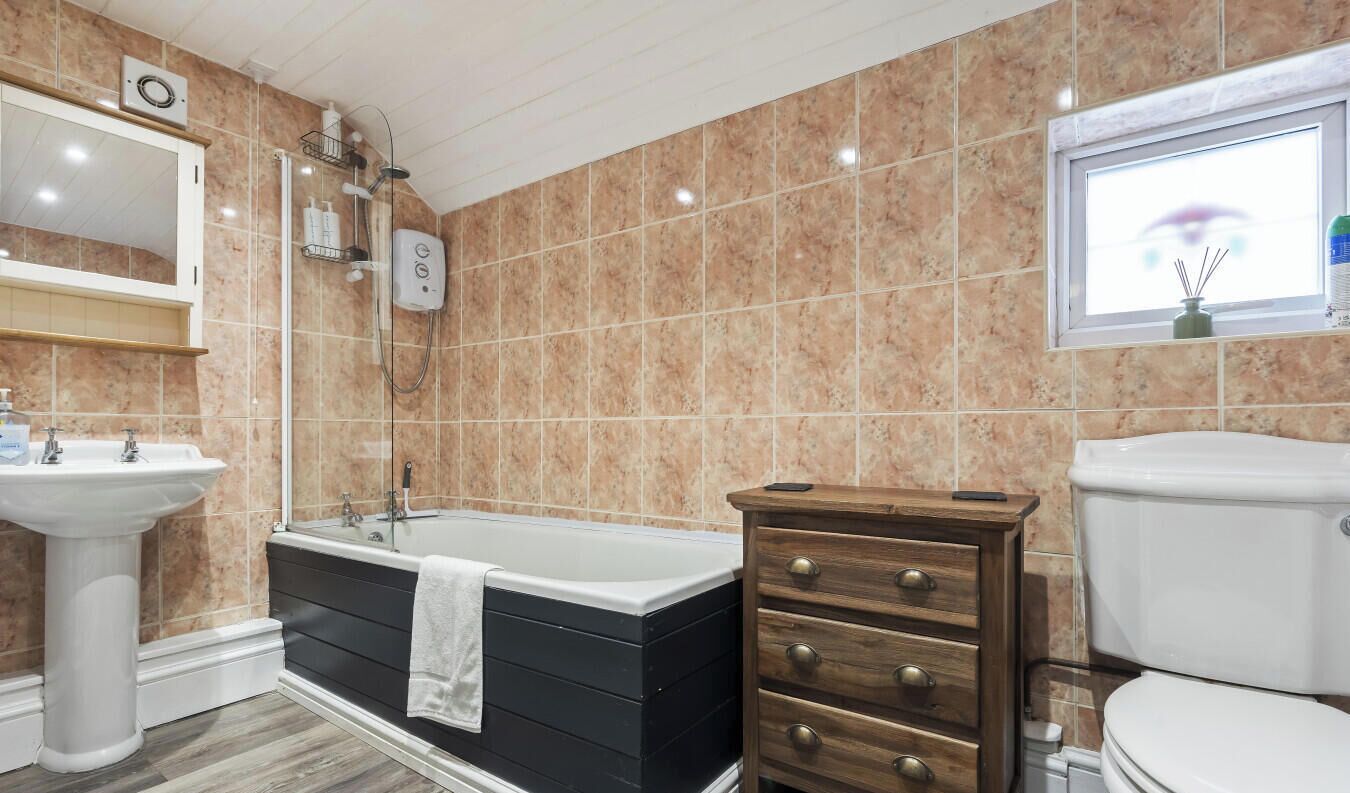 Un baño con bañera, lavamanos, inodoro, un armario de madera y una ventana con vistas.