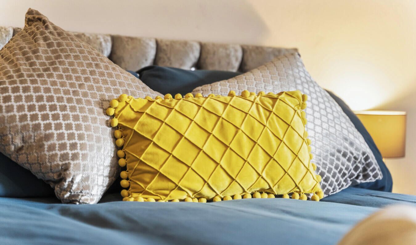 Una cama con una almohada estampada, una almohada acolchada amarilla y una colcha azul.