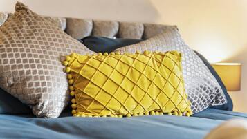 Una cama con una almohada estampada, una almohada acolchada amarilla y una colcha azul.