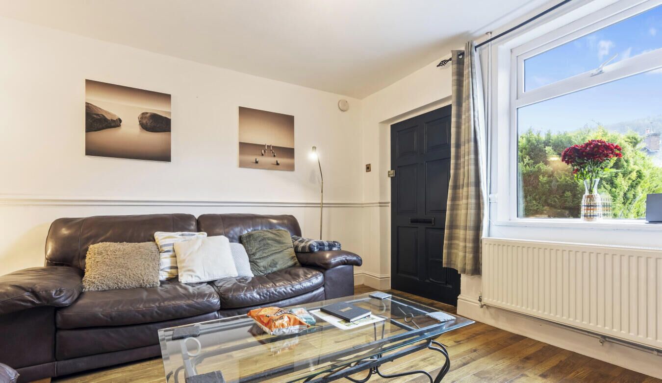 A living room with a leather sofa, a glass coffee table, and a view of a garden through a window.