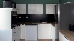 Eine kleine Küche mit weißen Schränken, einem Geschirrspüler, einer Mikrowelle und einem Kühlschrank.