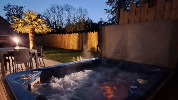 Ein Whirlpool mit Holzterrasse und Sitzgelegenheiten, umgeben von einem Holzzaun und Bäumen.