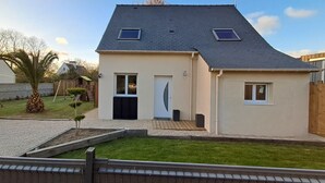 Ein eingeschossiges Haus mit geneigtem Dach, einer Haustür und zwei Fenstern.