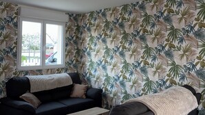 Ein Wohnzimmer mit einer schwarzen Couch, einem kleinen Sessel, einem Couchtisch und einem Fenster mit Blick auf Autos draußen.