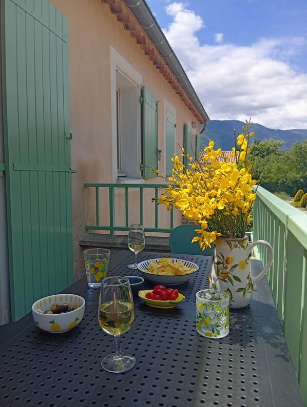 Ein Tisch mit Snacks, Getränken und einem Strauß gelber Blumen auf einem Balkon mit Bergblick.