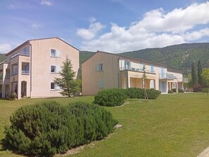Ein Wohngebäude mit mehreren Balkonen, einem gepflegten Rasen und einer Bergkulisse im Hintergrund.