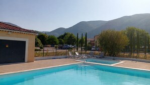 Ein Schwimmbad mit Liegestühlen, ein Gebäude mit Garage und Berge im Hintergrund.