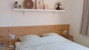 Ein Schlafzimmer mit einem hölzernen Kopfende, einem Bett mit gemusterten Betttextilien, Nachttischen mit Lampen und einem Regal mit Dekoration.