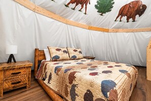A tent-style room with a bed, wooden nightstand, and a lamp. - Sunset Stampede Tepee | Dollywood | Resort Access (Sevierville)