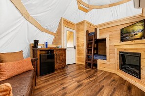 Ein Zeltinnenraum mit Holzboden, einer Couch, einer kleinen Küchenzeile, einem Kamin und einer Leiter.