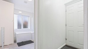 Ein Flur mit einer weißen Tür, einem Heizkörper, einem Fenster und einer Fußmatte.
