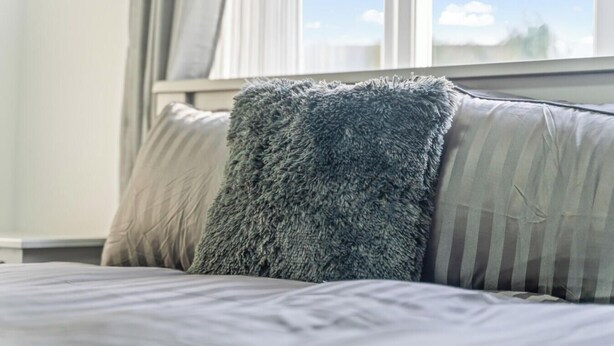 Ein Bett mit einem flauschigen, grauen Kissen und einem gestreiften Kissen.