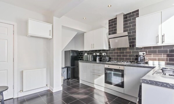 A modern kitchen with white cabinets, a black tiled backsplash, a built-in oven, and a countertop with a coffee machine. - Susan`s House - free on street parking! (Nottingham)
