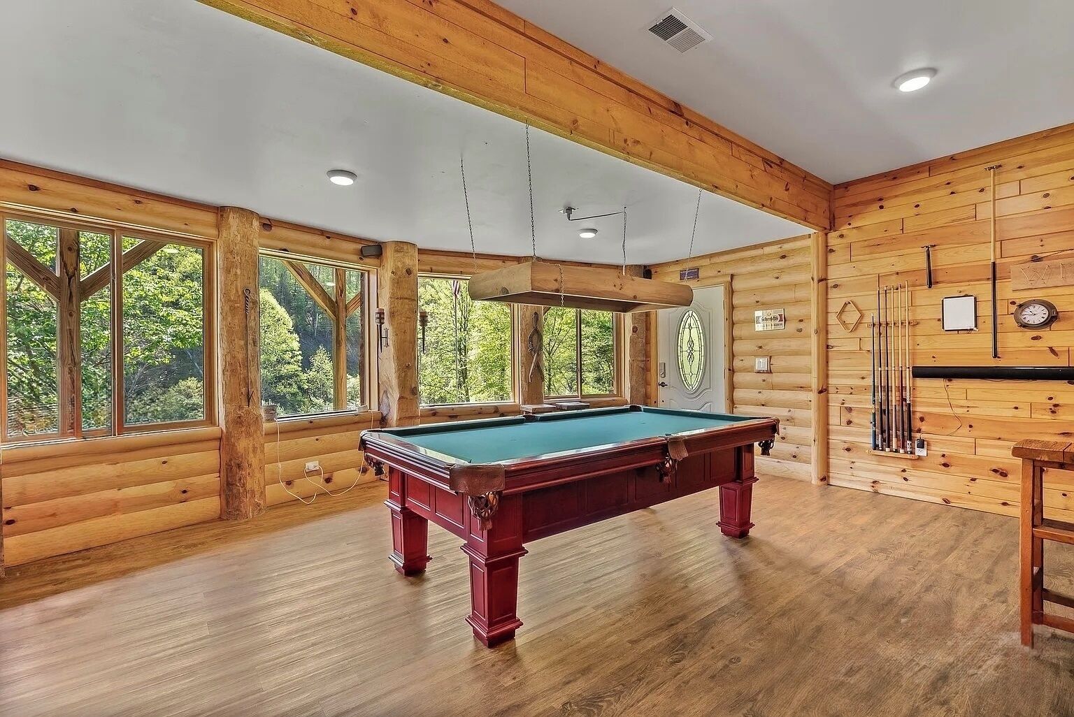 A pool table in a room with wooden walls and large windows.