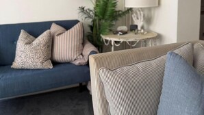 Ein Wohnzimmer mit blauem Sofa, einem gestreiften Sessel und einem kleinen runden Tisch mit Lampe.