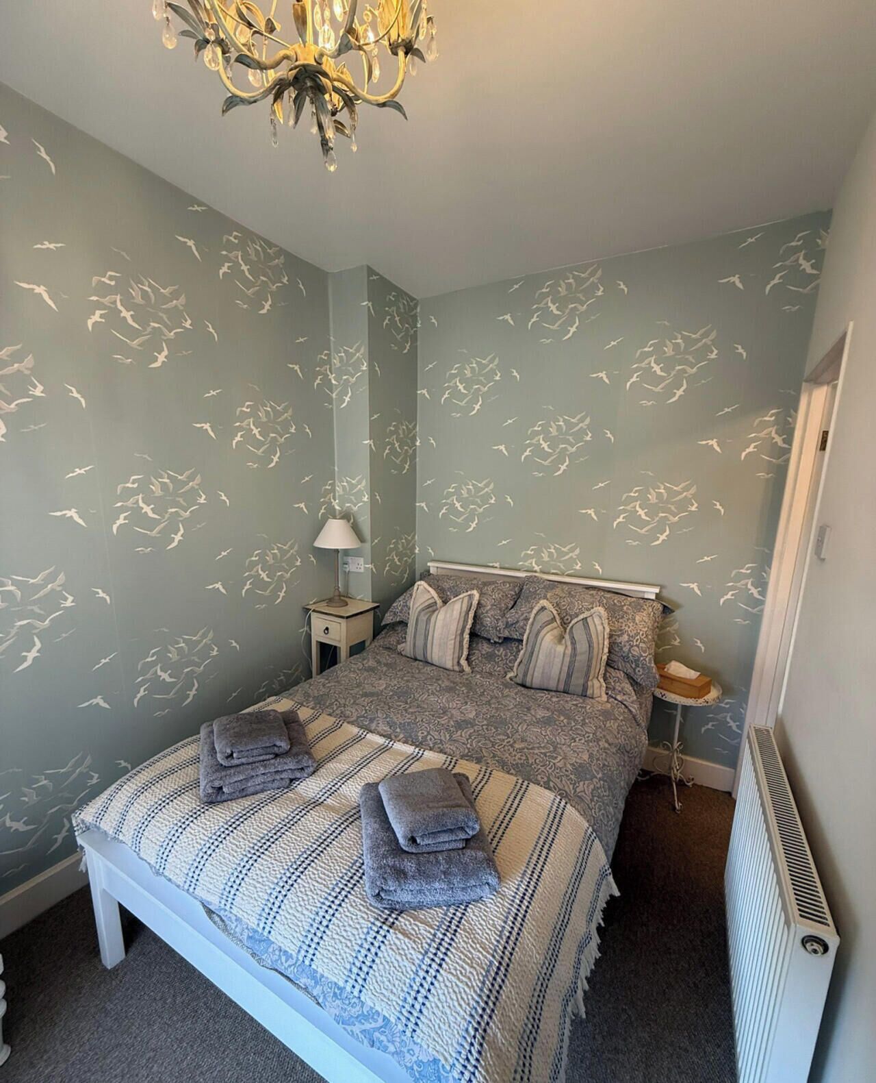 A bedroom with a bed, a nightstand, a lamp, and a radiator.