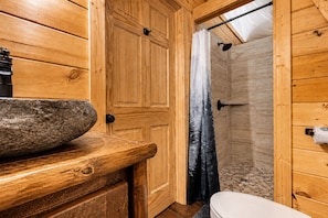 A wooden bathroom with a stone basin, a shower, and a toilet.