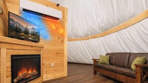 Ein gemütliches Interieur mit Kamin, einem an einer Holzwand montierten Fernseher und einer großen, weißen, zeltartigen Konstruktion.