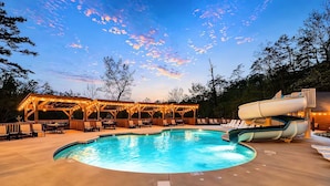A swimming pool with a slide, surrounded by a wooden deck and lounge chairs.